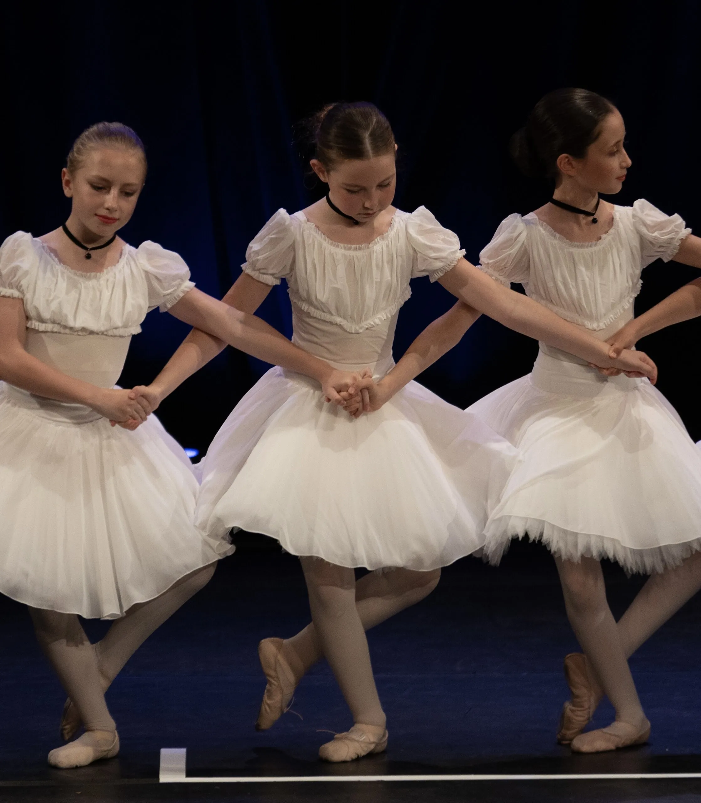 Trois élèves en tutu blanc sur scène.