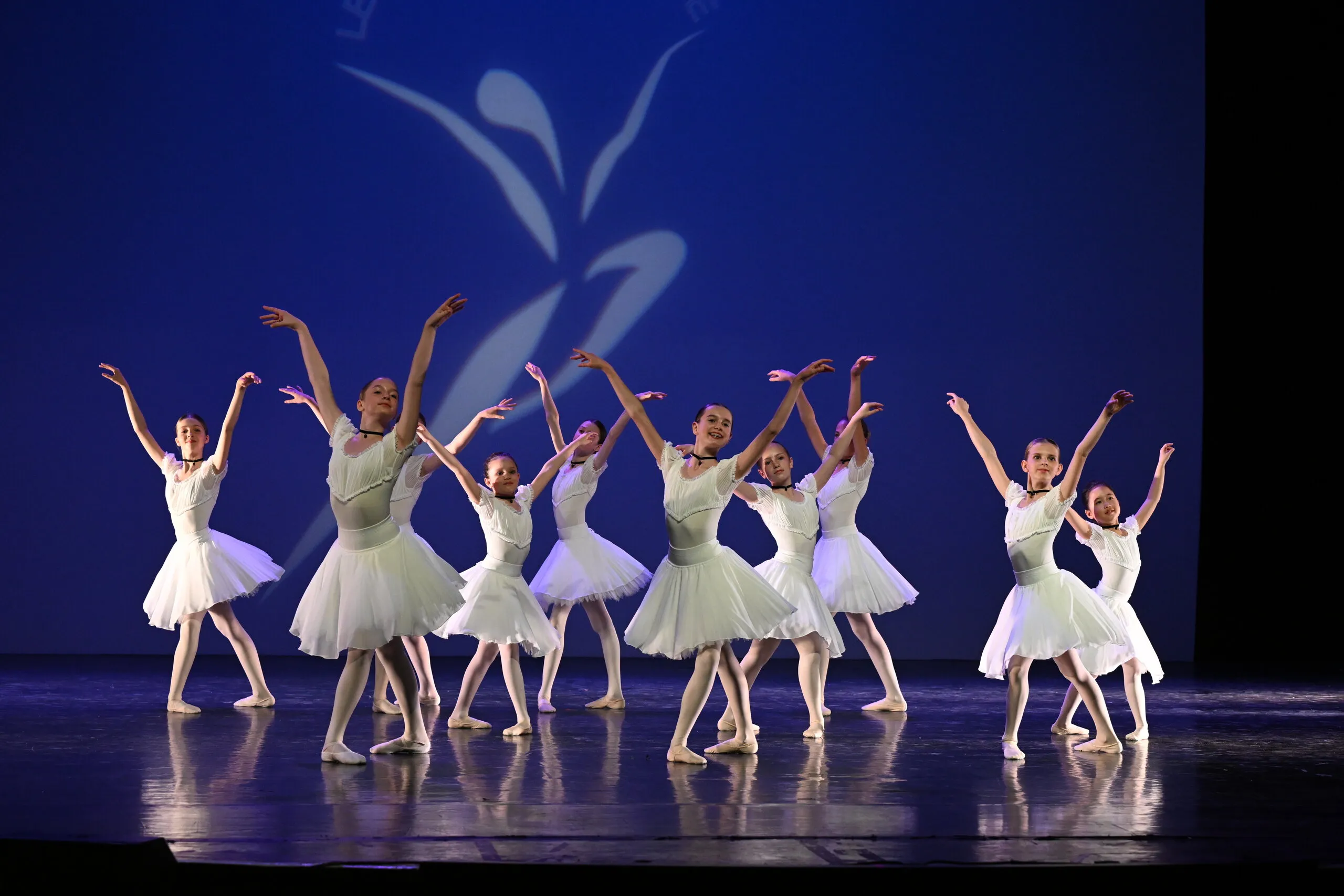 Groupe d'élèves en tutu blanc, les bras levés.