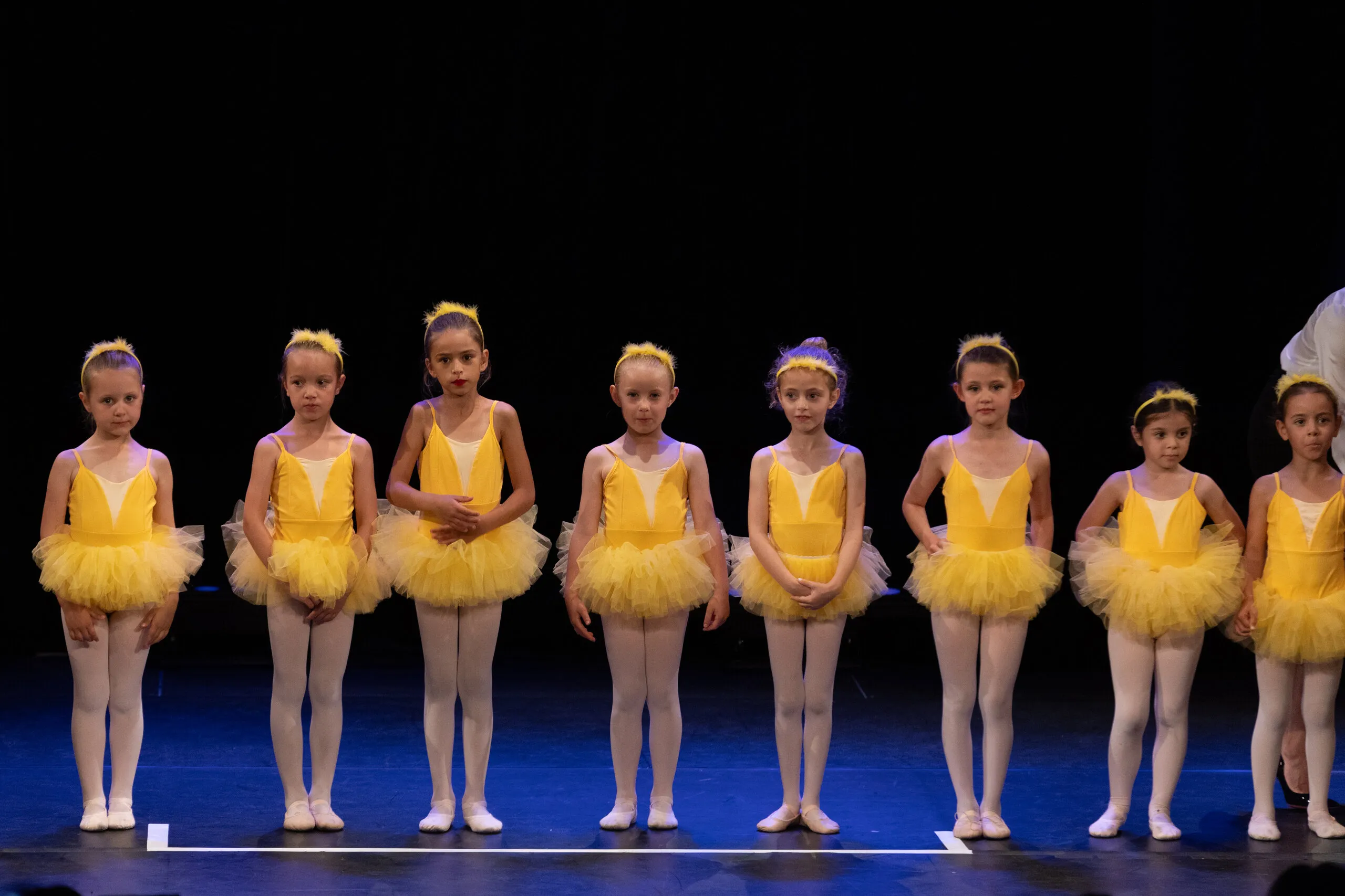 Ligne de jeunes élèves en tutu jaune sur la scène.