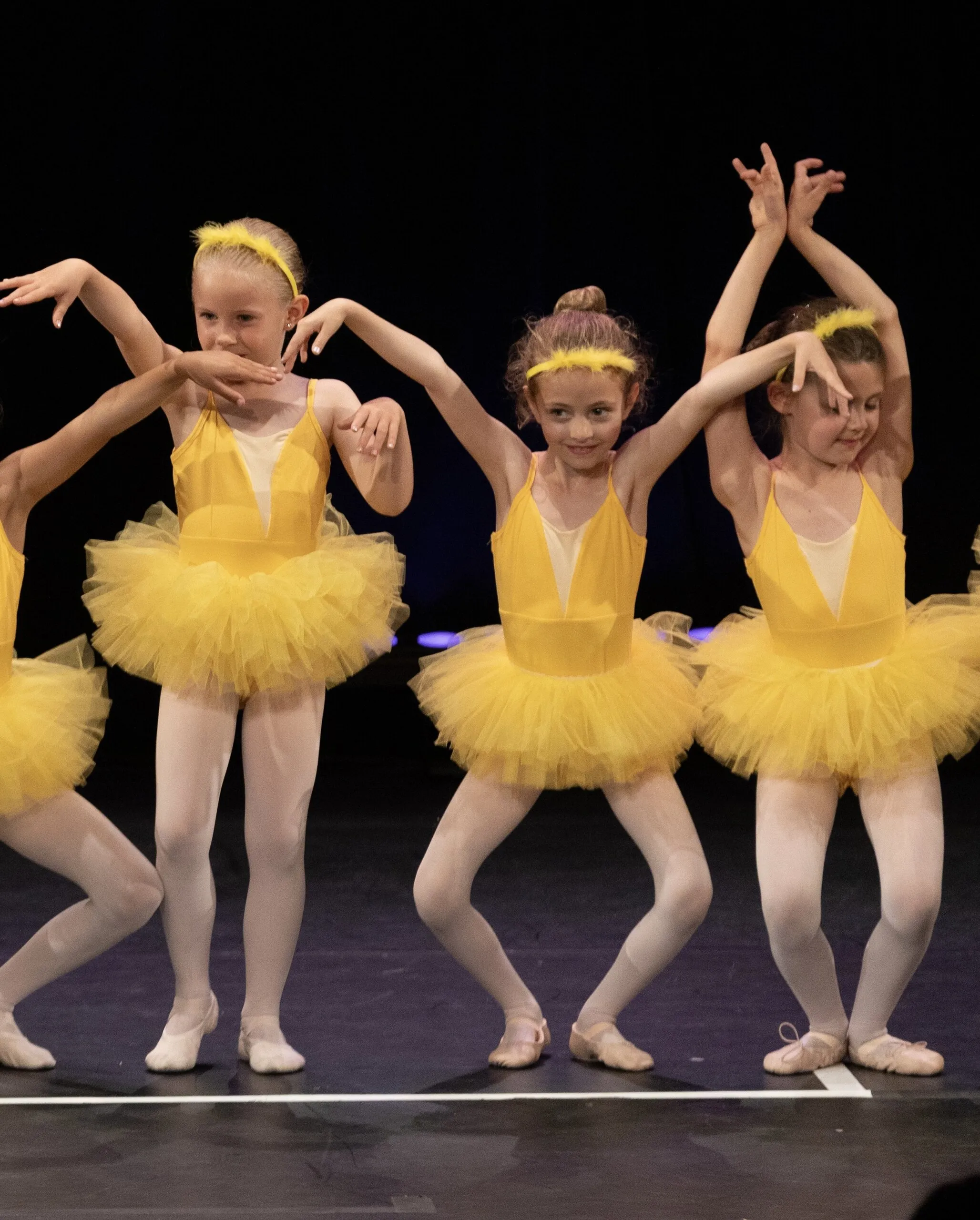 Trois jeunes élèves en tutu jaune, en position.