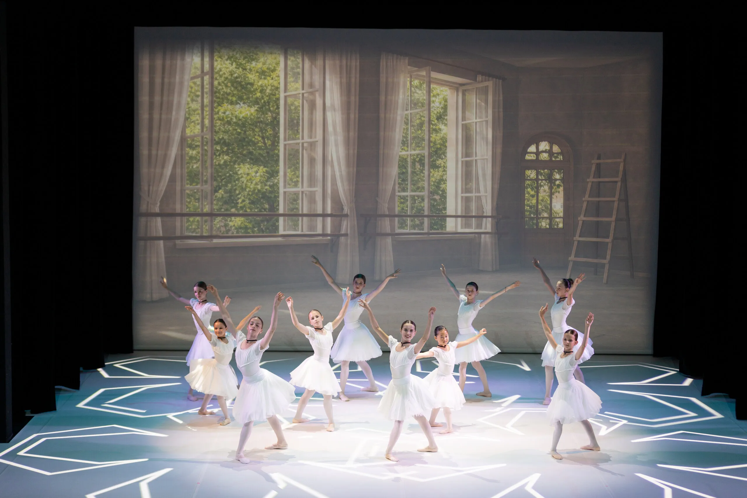 Groupe de tutus blancs devant le décor de fenêtres.