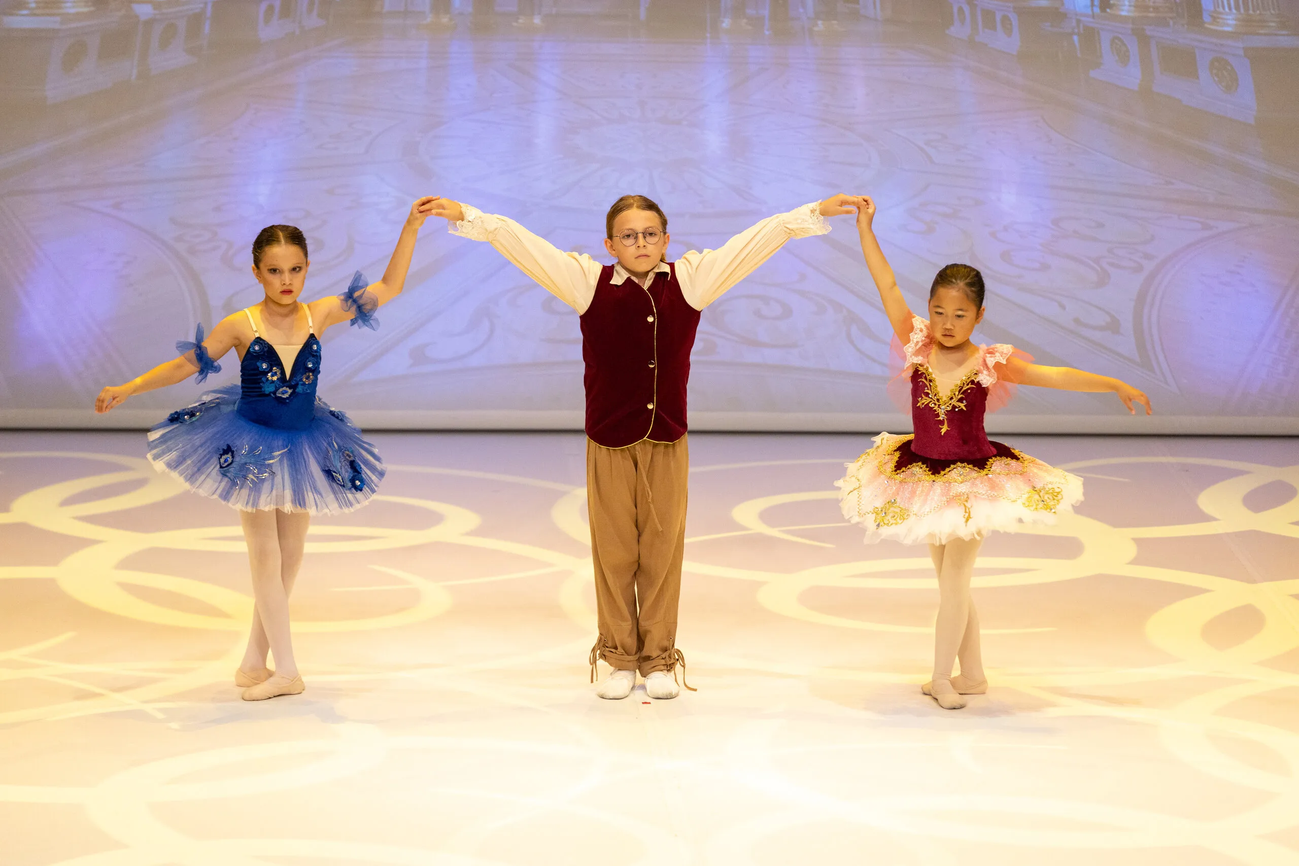 Trois jeunes élèves main dans la main, tutus bleu et bordeaux.