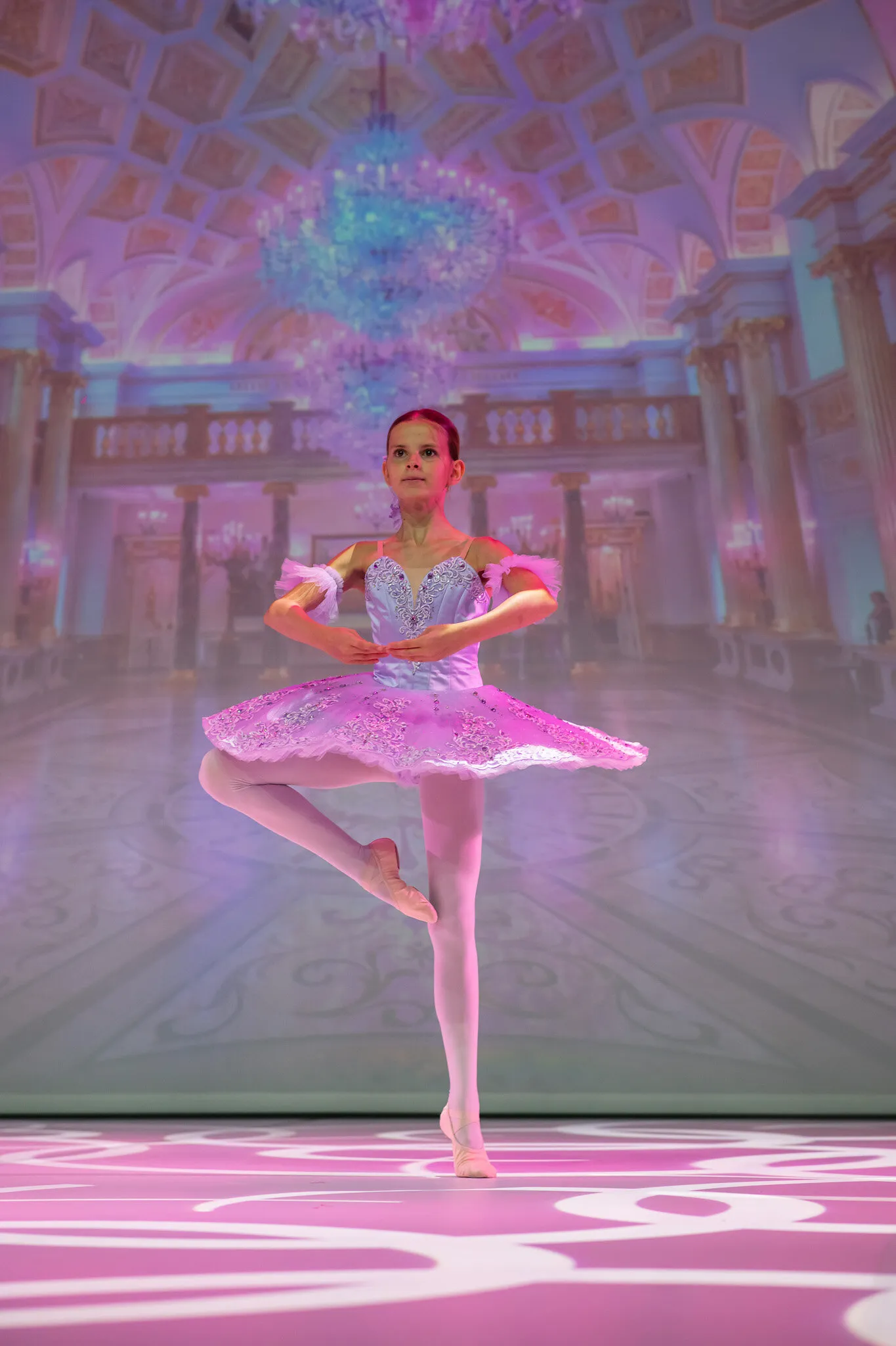 Une élève en tutu rose, en retiré devant le décor du palais.