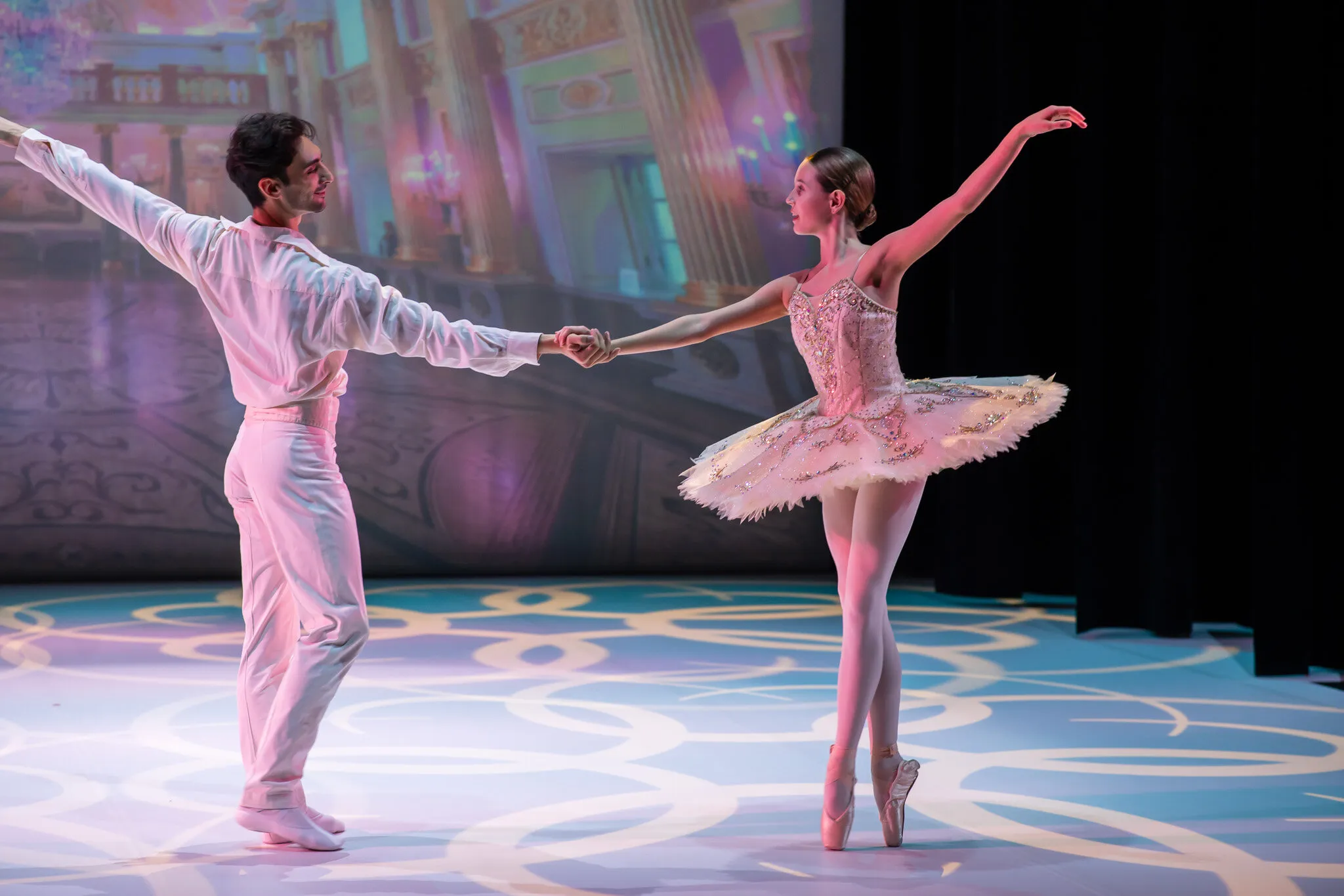 Pendant la générale, une jeune ballerine en tutu rose pâle sur les pointes, la main tenue à bout de bras par son partenaire en blanc.