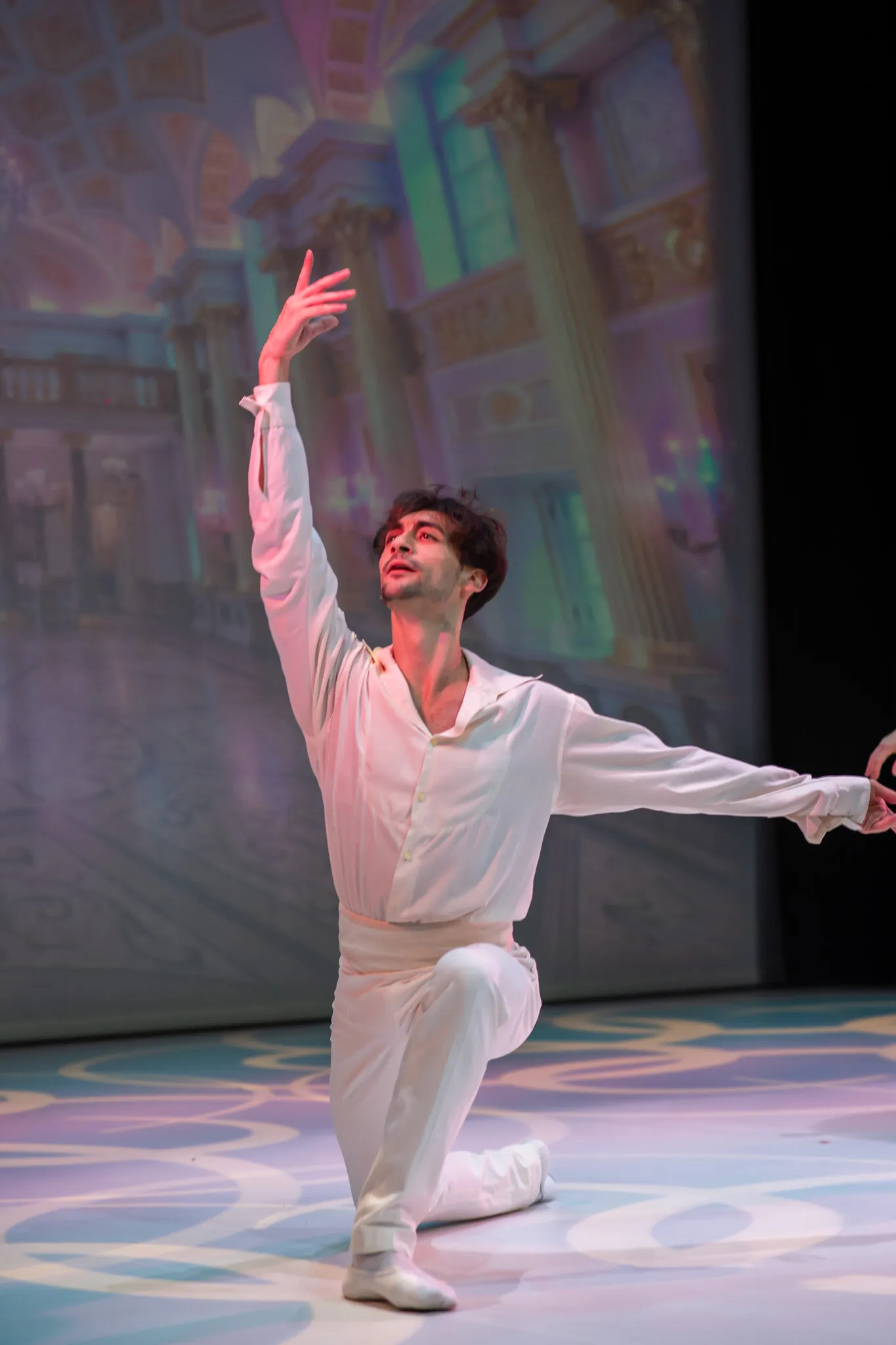 Le danseur en blanc seul, un genou à terre et le bras levé, devant le décor du palais.