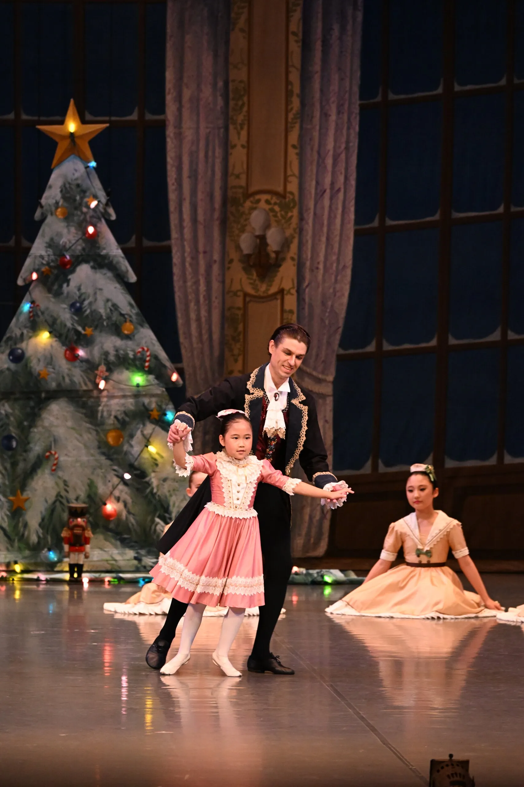 Une élève en robe rose, menée dans la danse près du sapin illuminé.