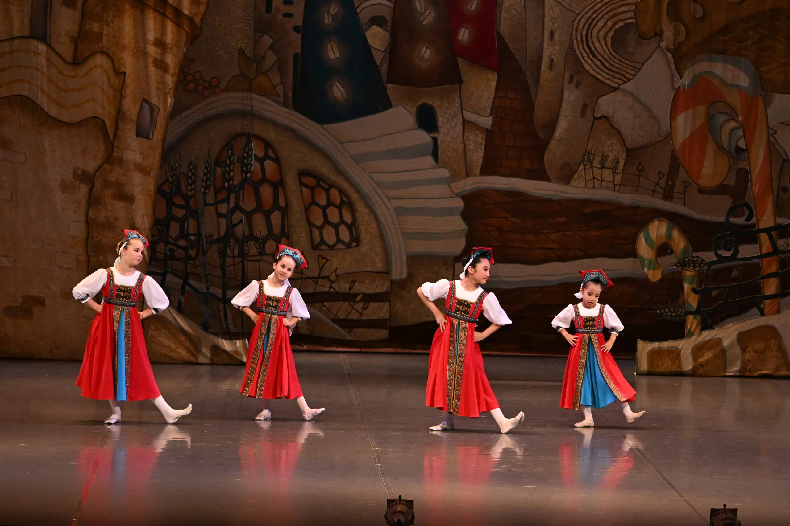 Quatre élèves en costumes de caractère rouges, en ligne devant le décor.