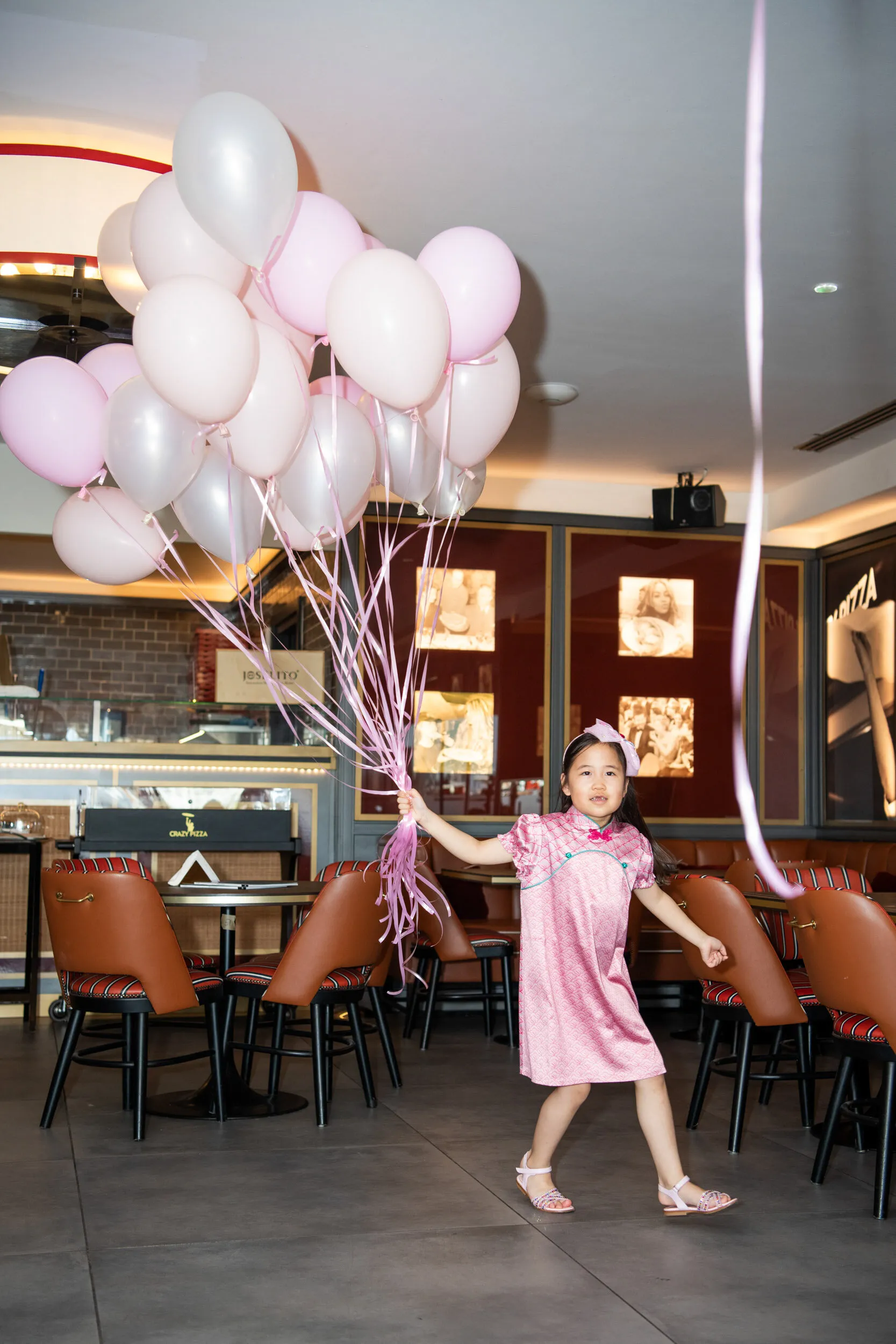 Une enfant traverse la salle avec un grand bouquet de ballons roses.