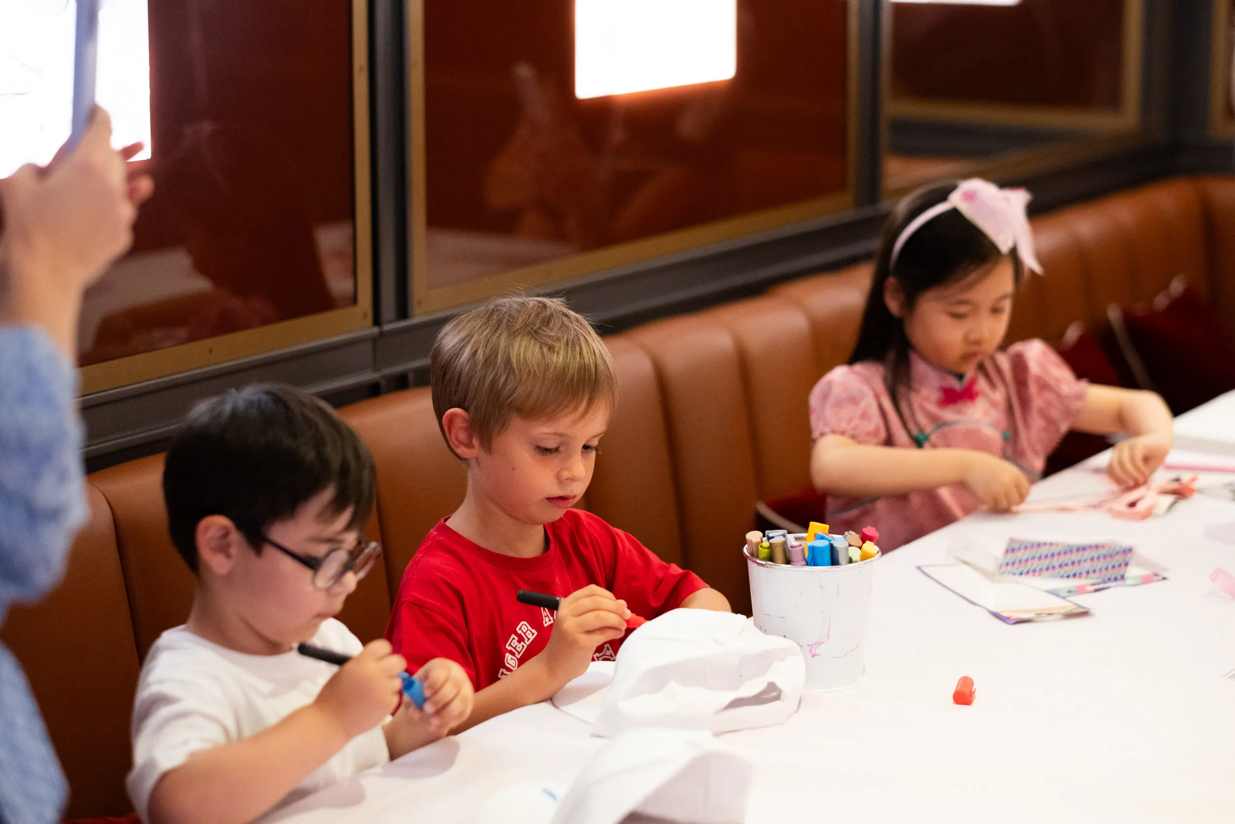 Trois enfants concentrés décorent leurs casquettes à la table d'atelier.