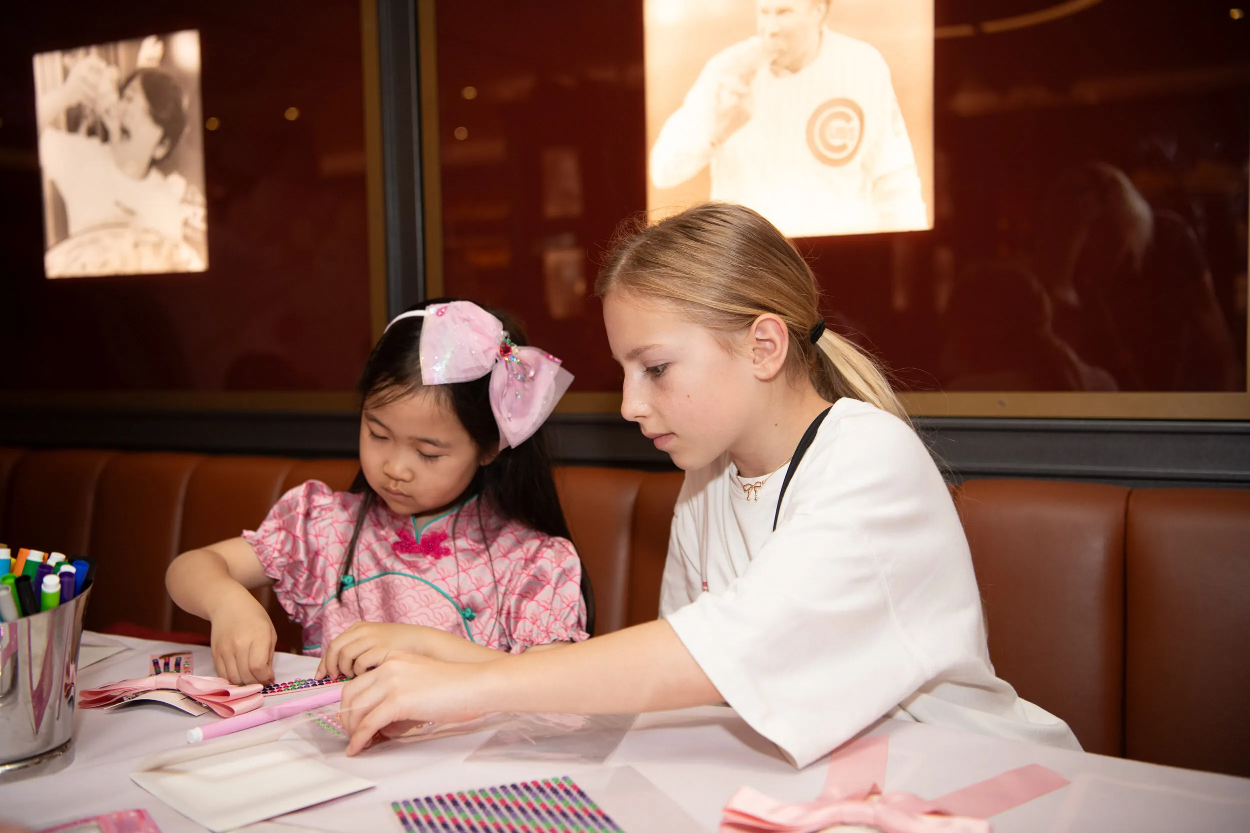 Deux enfants assemblent rubans et strass à la table d'atelier.
