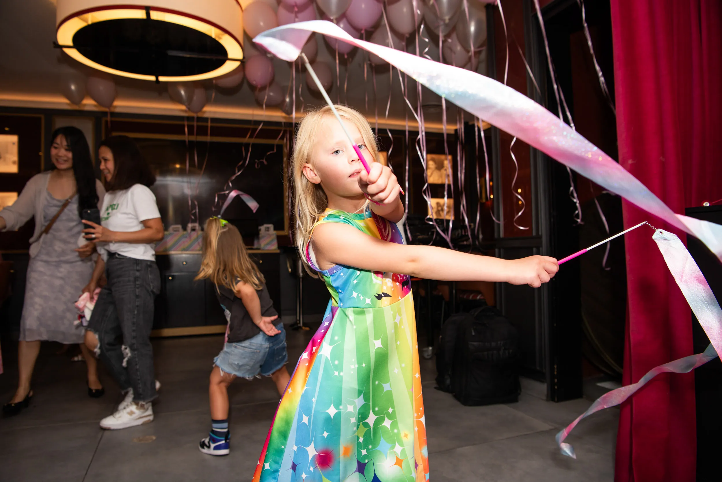 Une enfant fait tournoyer deux longs rubans dans la salle décorée de ballons.