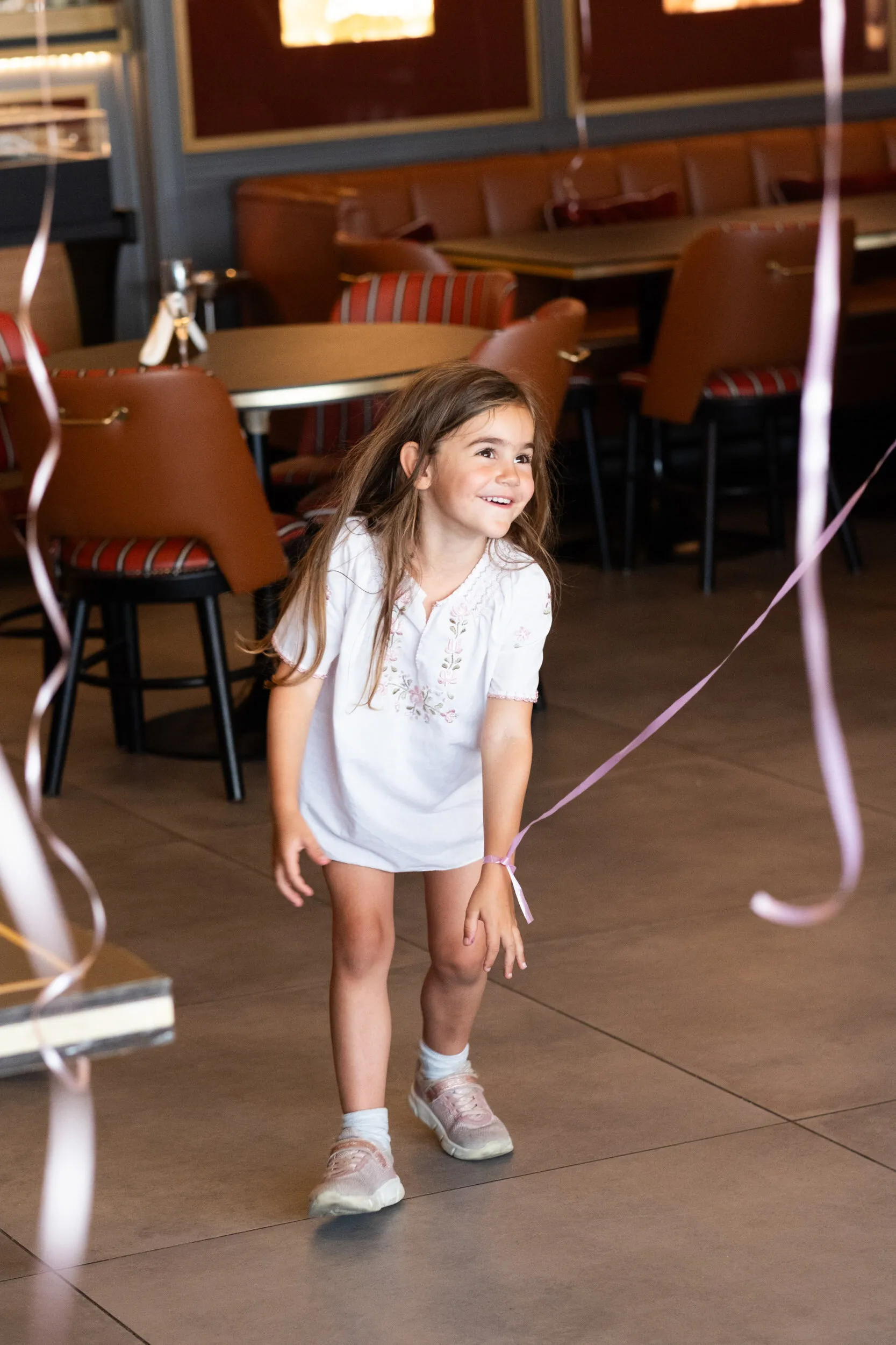 Une enfant rit en dansant, un ruban de ballon noué au poignet.