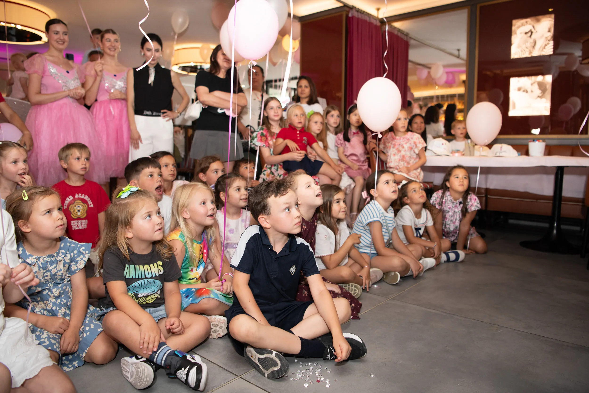 Les enfants assis en tailleur suivent le spectacle, entourés des familles.
