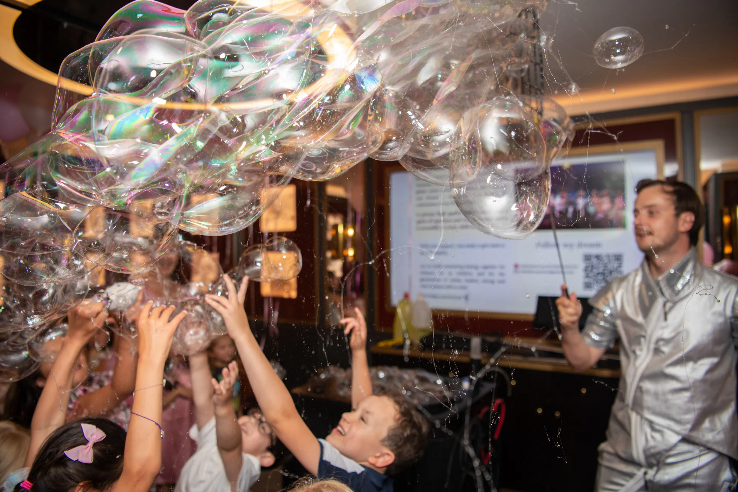 Des mains d'enfants tendues vers une cascade de bulles irisées.
