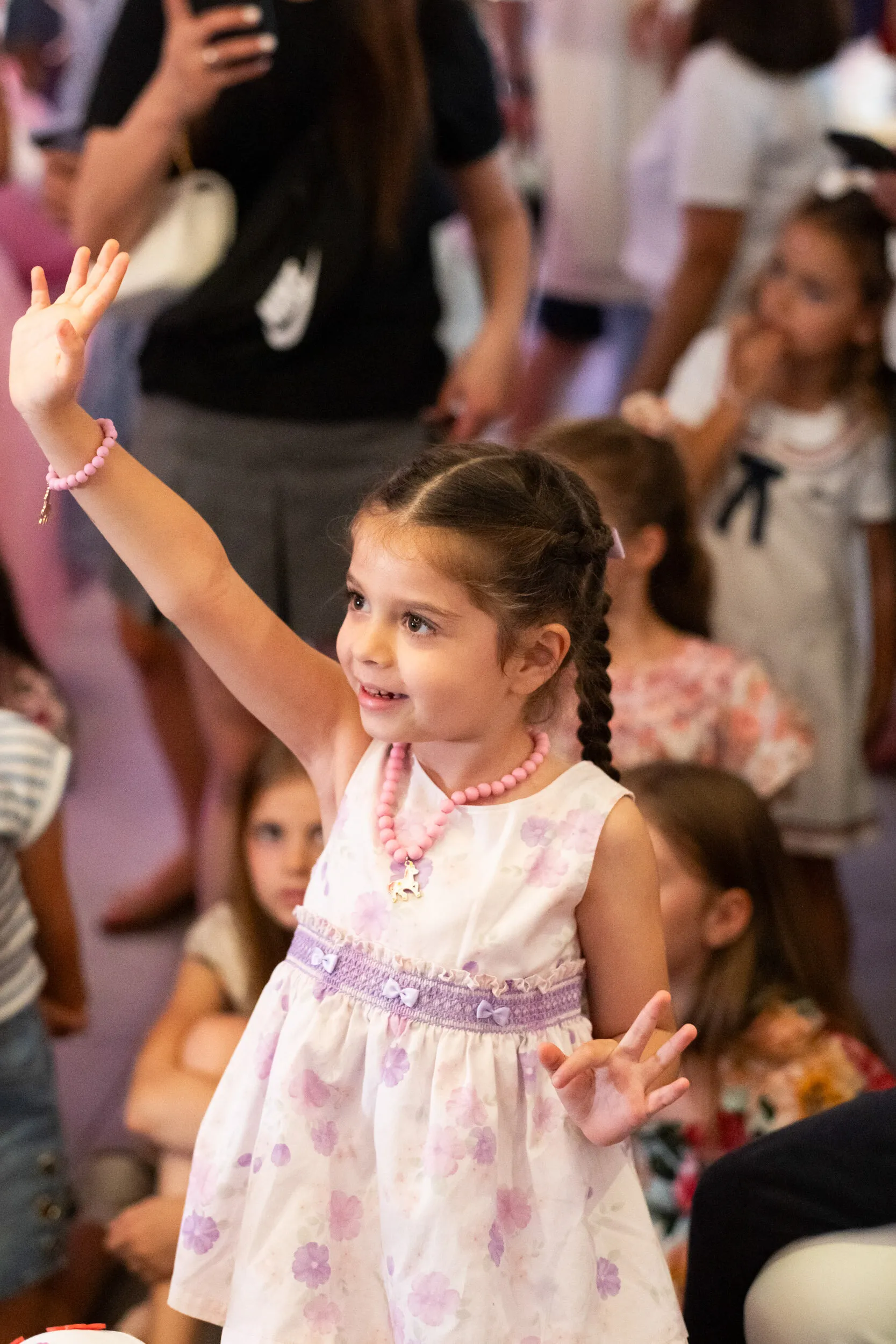 Une enfant lève la main au milieu du public, le sourire aux lèvres.