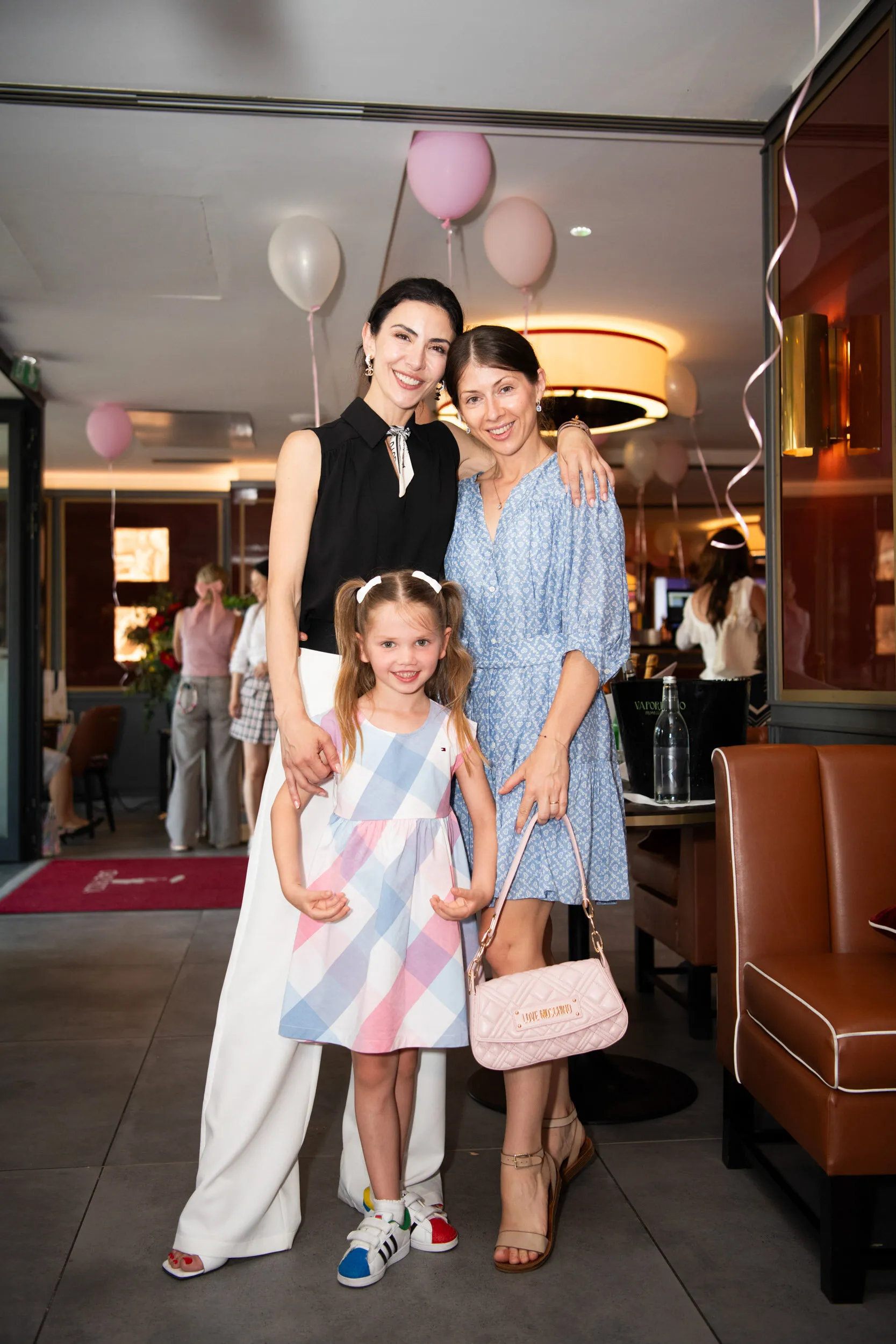 La fondatrice pose avec une enfant et une invitée à l'entrée de la salle.