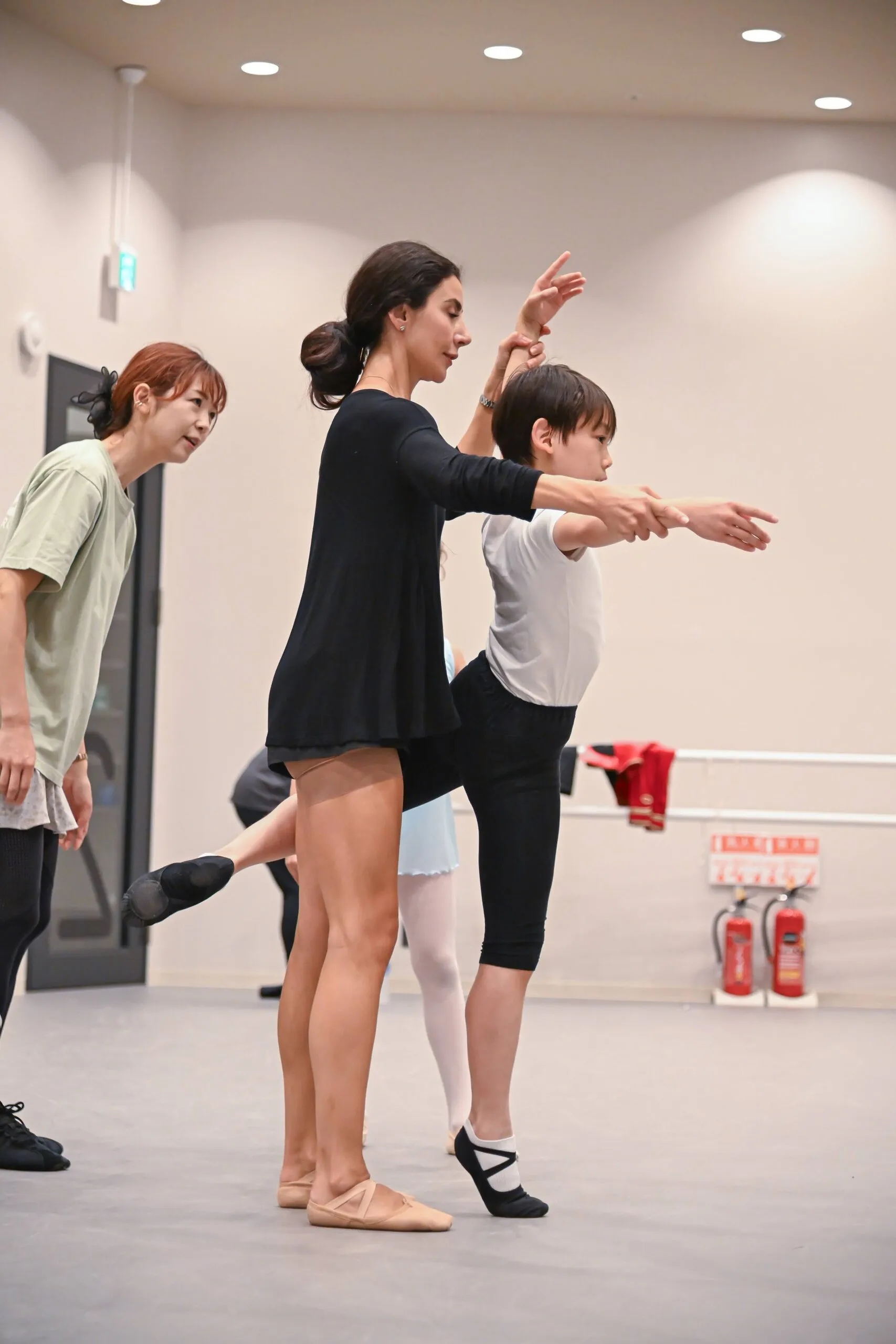 Deux professeures accompagnent l'arabesque d'un jeune élève.